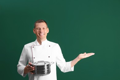 Happy male chef with cooking pot on dark green background. Space for text Photo of Happy male chef with cooking pot on dark green background. Space for text