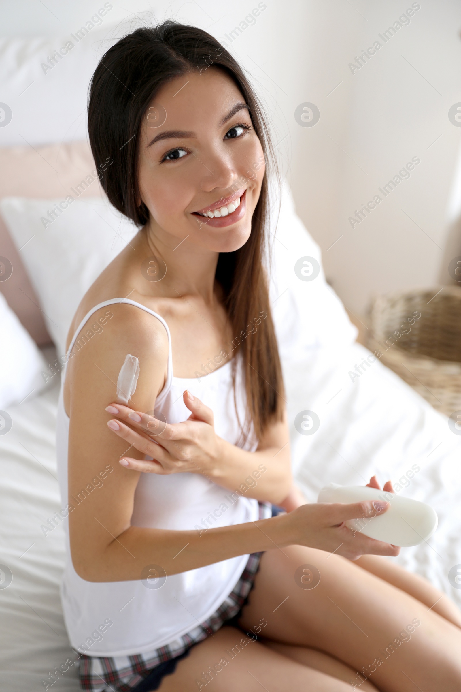 Beautiful young woman applying body cream in bedroom Photo of Beautiful young woman applying body cream in bedroom