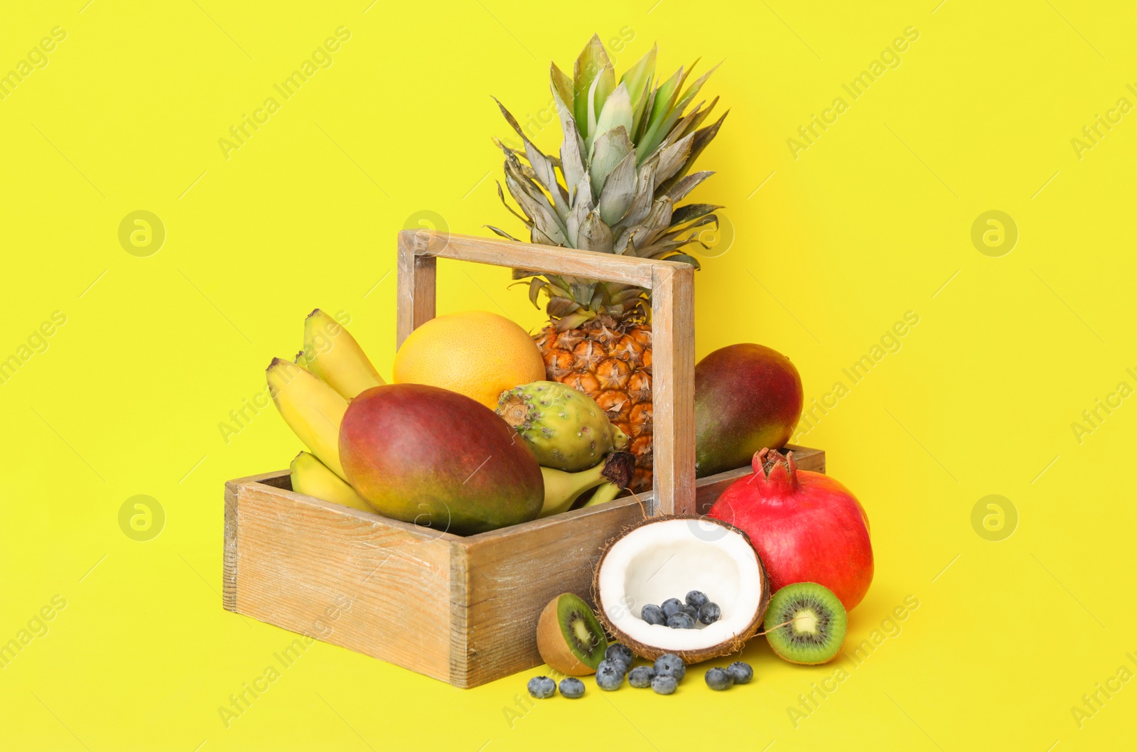 Assortment of fresh exotic fruits in crate on yellow background Photo of Assortment of fresh exotic fruits in crate on yellow background
