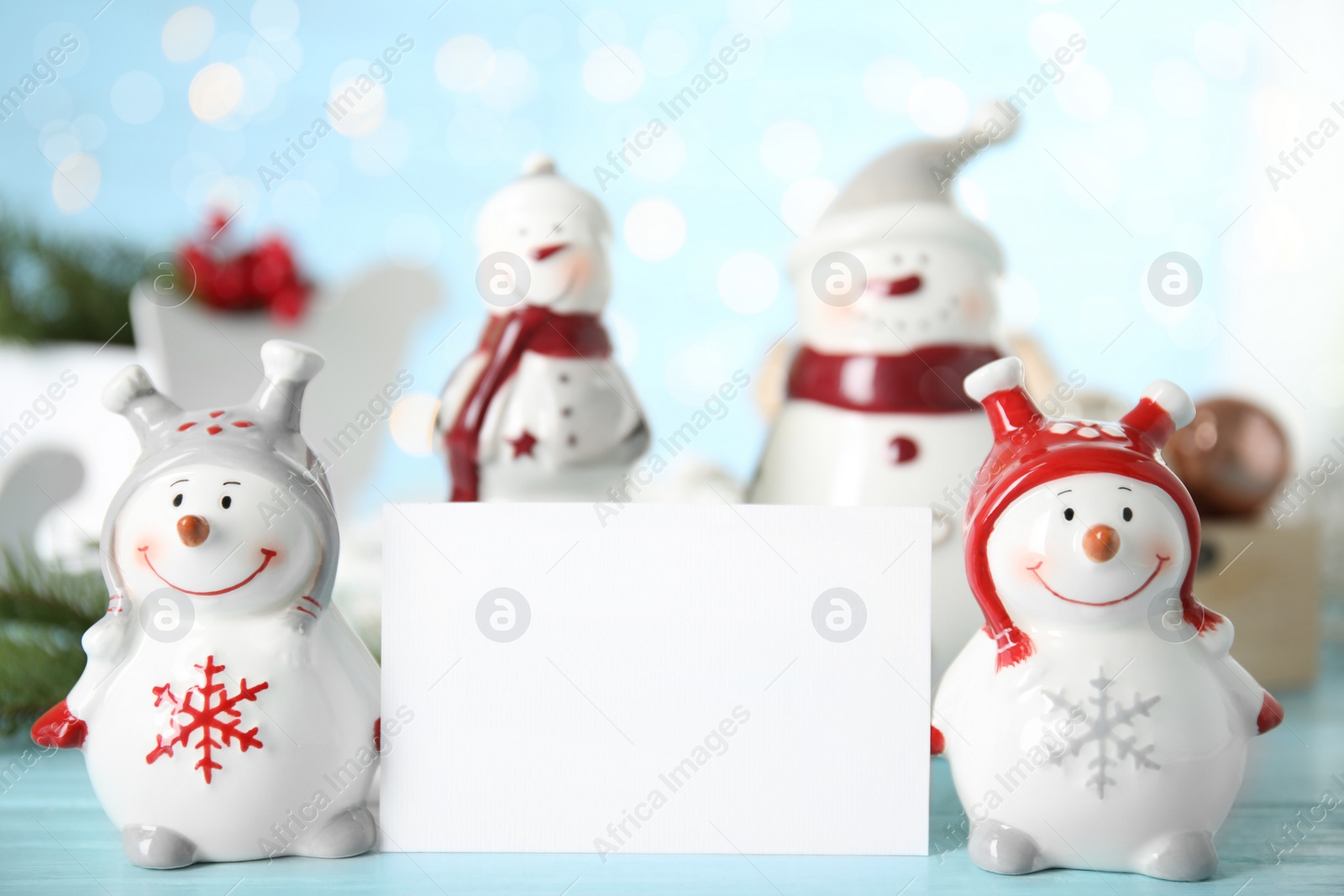 Decorative snowmen near blank white card on light blue table, space for text Photo of Decorative snowmen near blank white card on light blue table, space for text