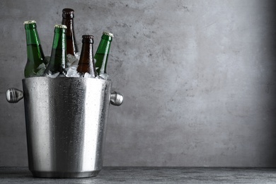 Metal bucket with bottles of beer and ice cubes on grey table, space for text Photo of Metal bucket with bottles of beer and ice cubes on grey table, space for text