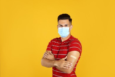 Vaccinated man with protective mask and medical plaster on his arm against yellow background Photo of Vaccinated man with protective mask and medical plaster on his arm against yellow background