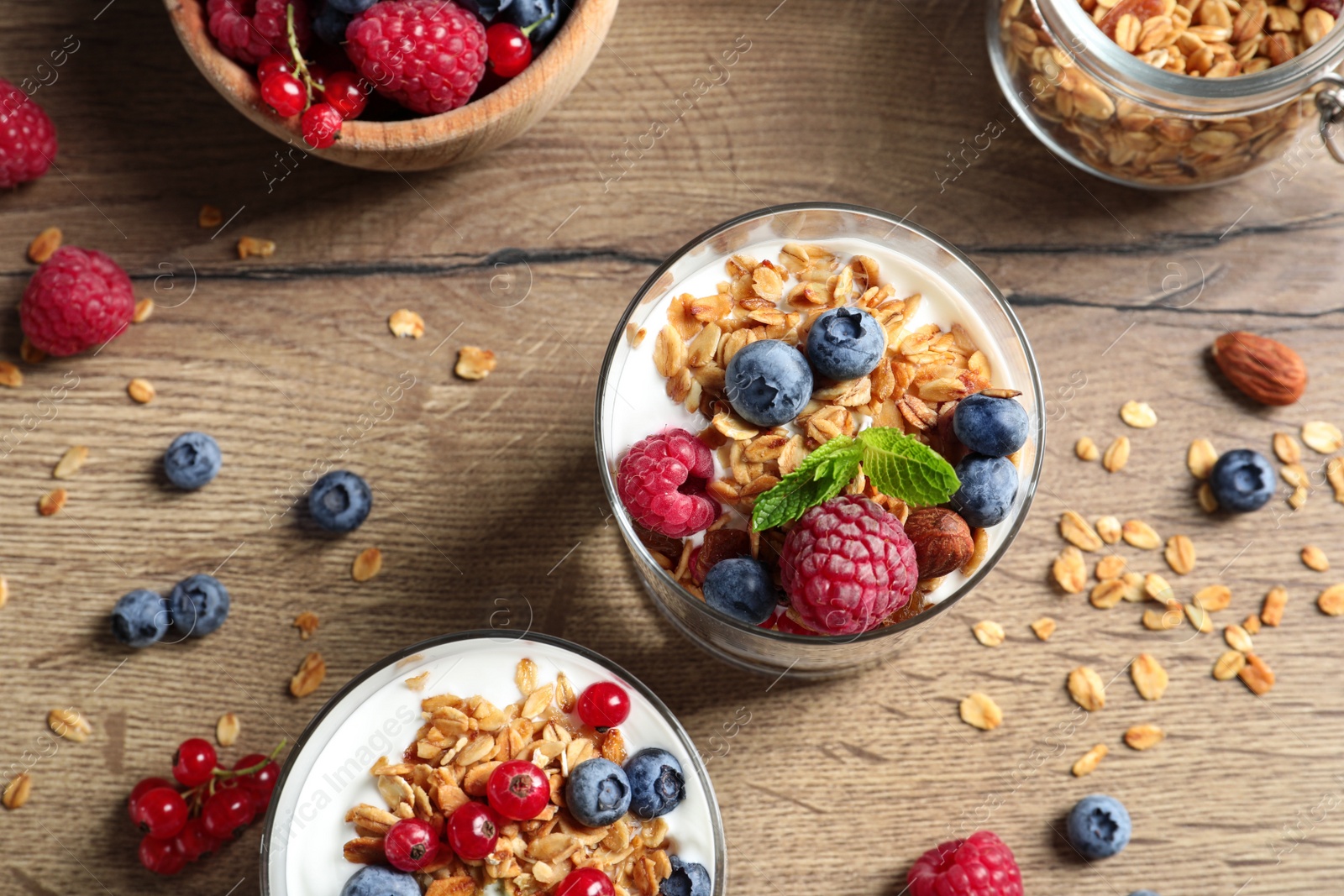 Tasty dessert with yogurt, berries and granola on wooden table, flat lay Image of Tasty dessert with yogurt, berries and granola on wooden table, flat lay