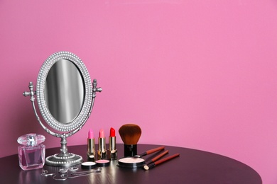 Stylish mirror, makeup products and accessories on table near color wall Photo of Stylish mirror, makeup products and accessories on table near color wall