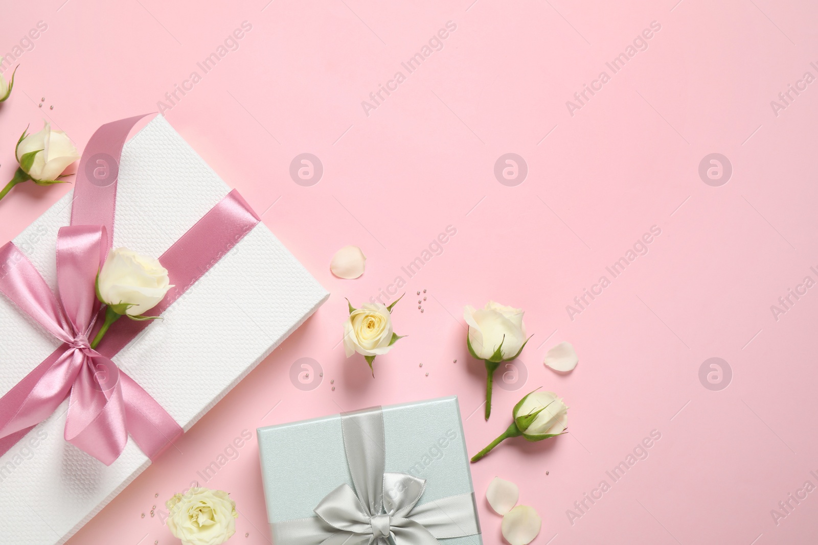 Elegant gift boxes and beautiful flowers on pink background, flat lay. Space for text Photo of Elegant gift boxes and beautiful flowers on pink background, flat lay. Space for text