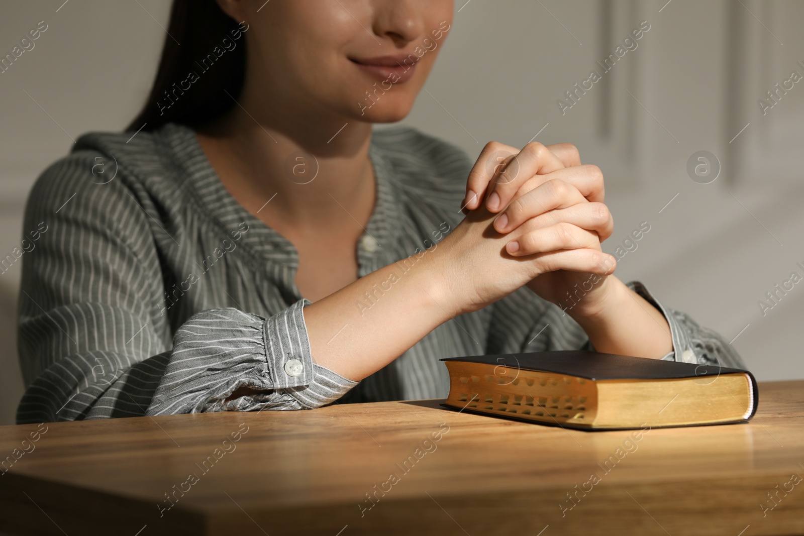 Religious woman praying over Bible at wooden table indoors, closeup Photo of Religious woman praying over Bible at wooden table indoors, closeup