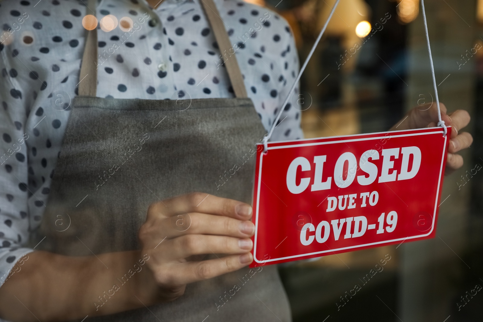 Woman in mask putting red sign with words Closed Due To Covid-19 hanging onto glass door, closeup Photo of Woman in mask putting red sign with words Closed Due To Covid-19 hanging onto glass door, closeup