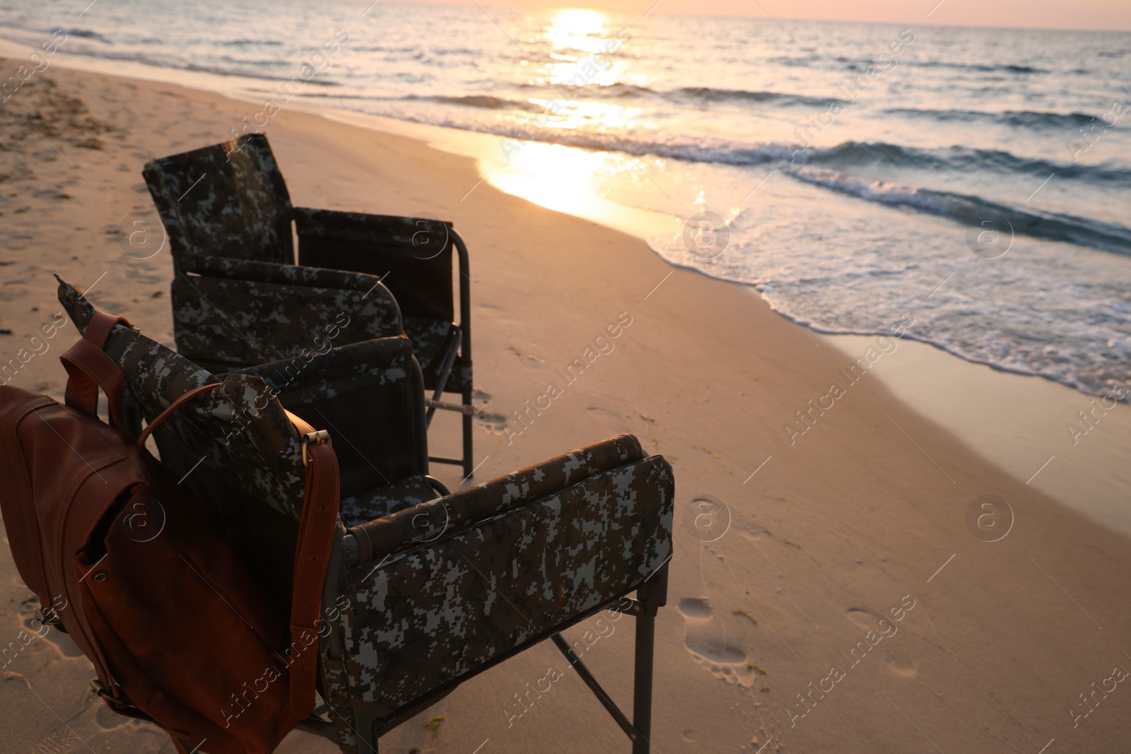 Camping chairs and backpack on sandy beach near sea, space for text Photo of Camping chairs and backpack on sandy beach near sea, space for text