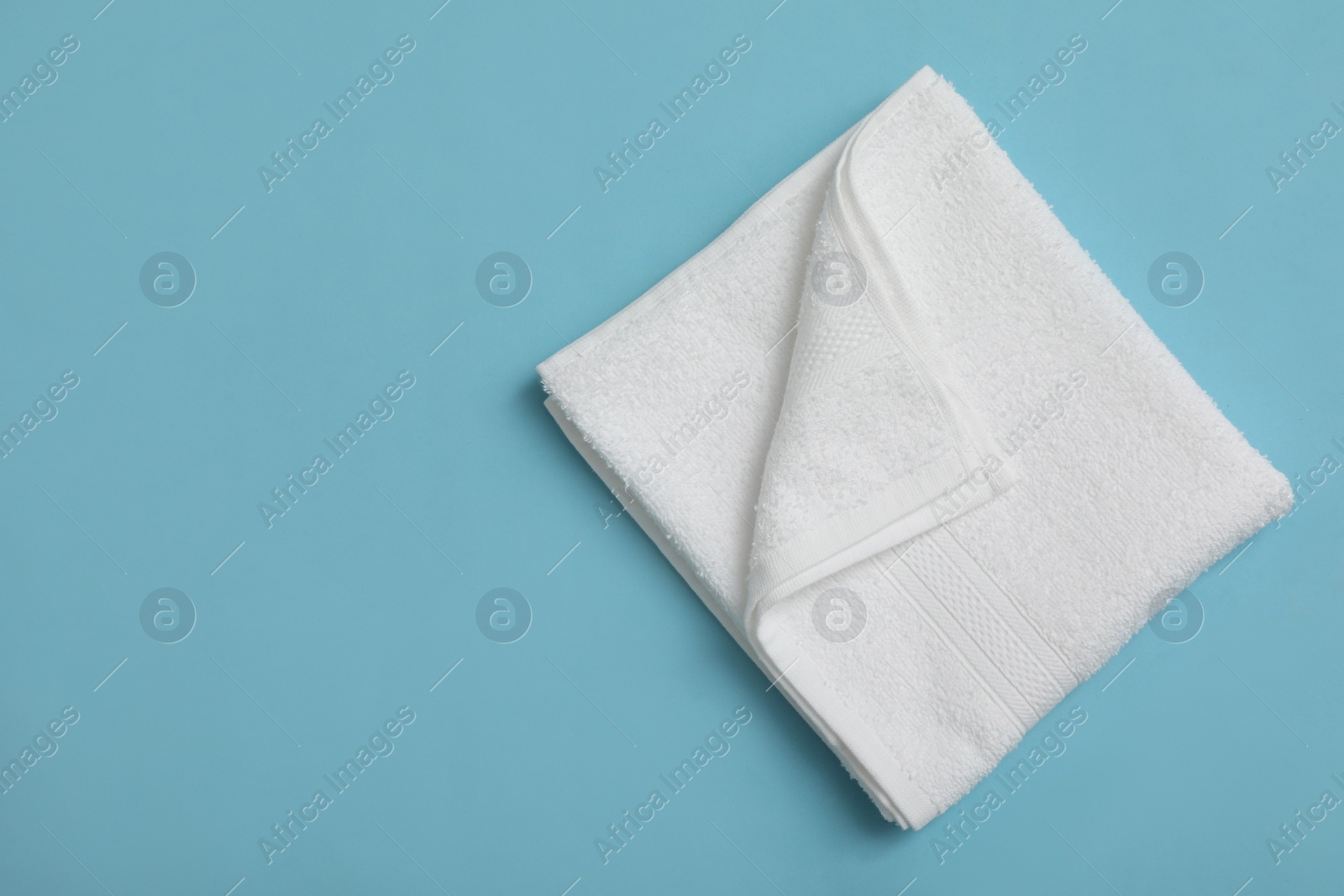 Folded white beach towel on light blue background, top view. Space for text Photo of Folded white beach towel on light blue background, top view. Space for text