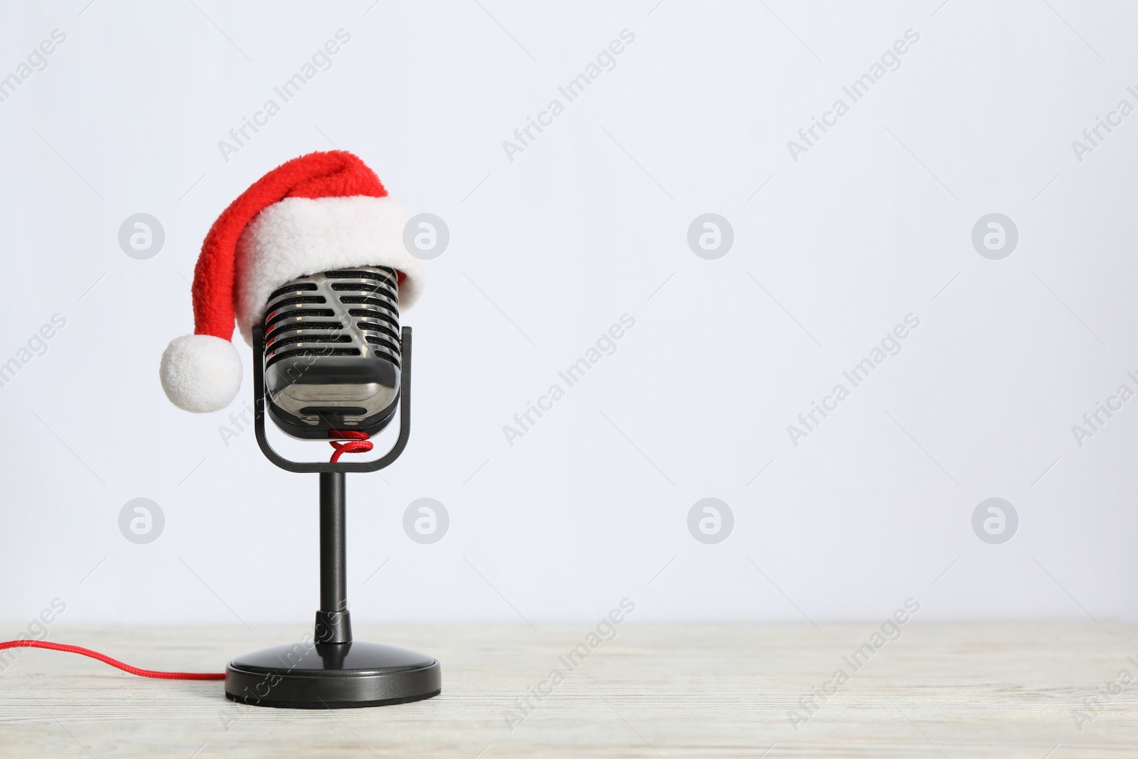 Retro microphone with Santa hat on wooden table against white background, space for text. Christmas music Photo of Retro microphone with Santa hat on wooden table against white background, space for text. Christmas music