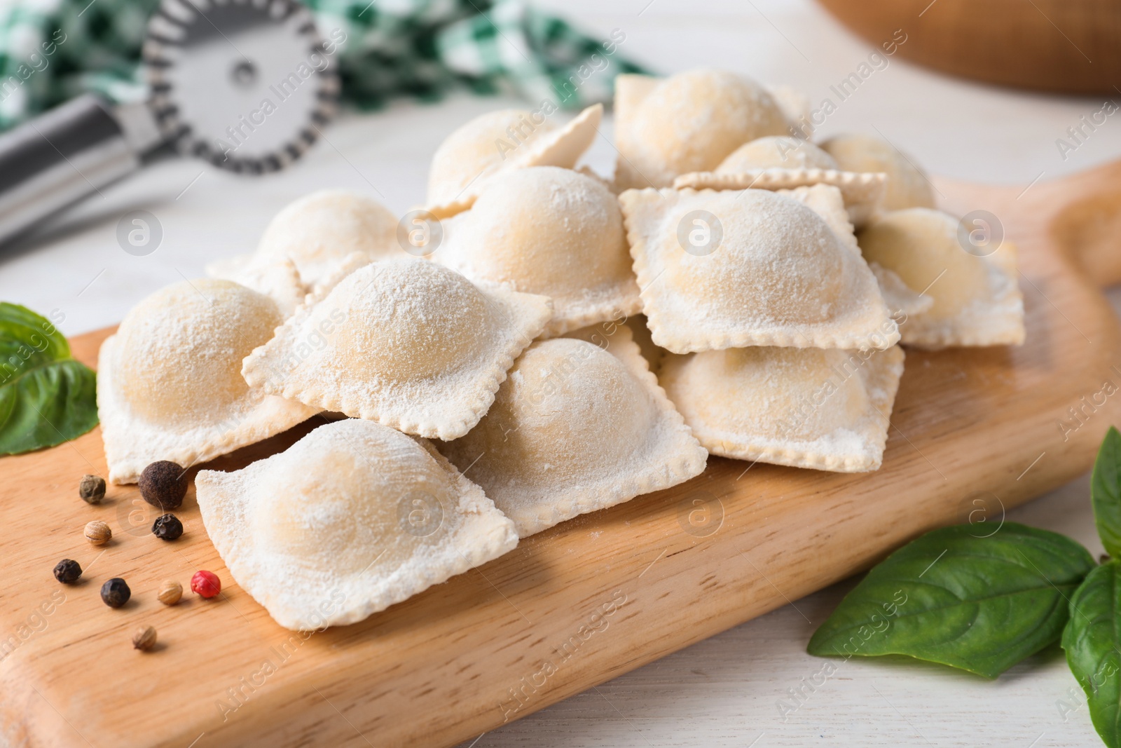 Photo of Uncooked ravioli, peppercorns and basil on white wooden table, closeup