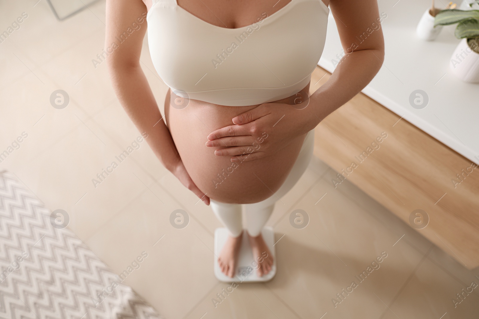Pregnant woman standing on scales at home, above view Photo of Pregnant woman standing on scales at home, above view