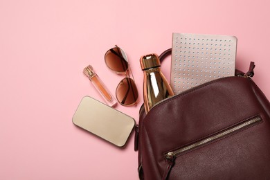 Stylish urban backpack with different items on light pink background, flat lay Photo of Stylish urban backpack with different items on light pink background, flat lay