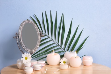 Stylish mirror, cosmetic products and aroma candles on table near light wall Photo of Stylish mirror, cosmetic products and aroma candles on table near light wall