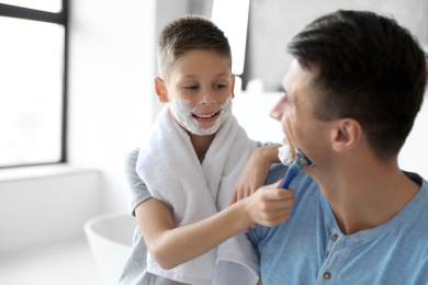 Son shaving his father with razor in bathroom Photo of Son shaving his father with razor in bathroom