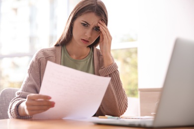 Worried woman reading letter at wooden table in room Photo of Worried woman reading letter at wooden table in room