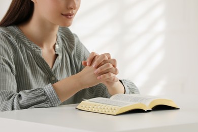Religious woman praying over Bible at table indoors, closeup Photo of Religious woman praying over Bible at table indoors, closeup