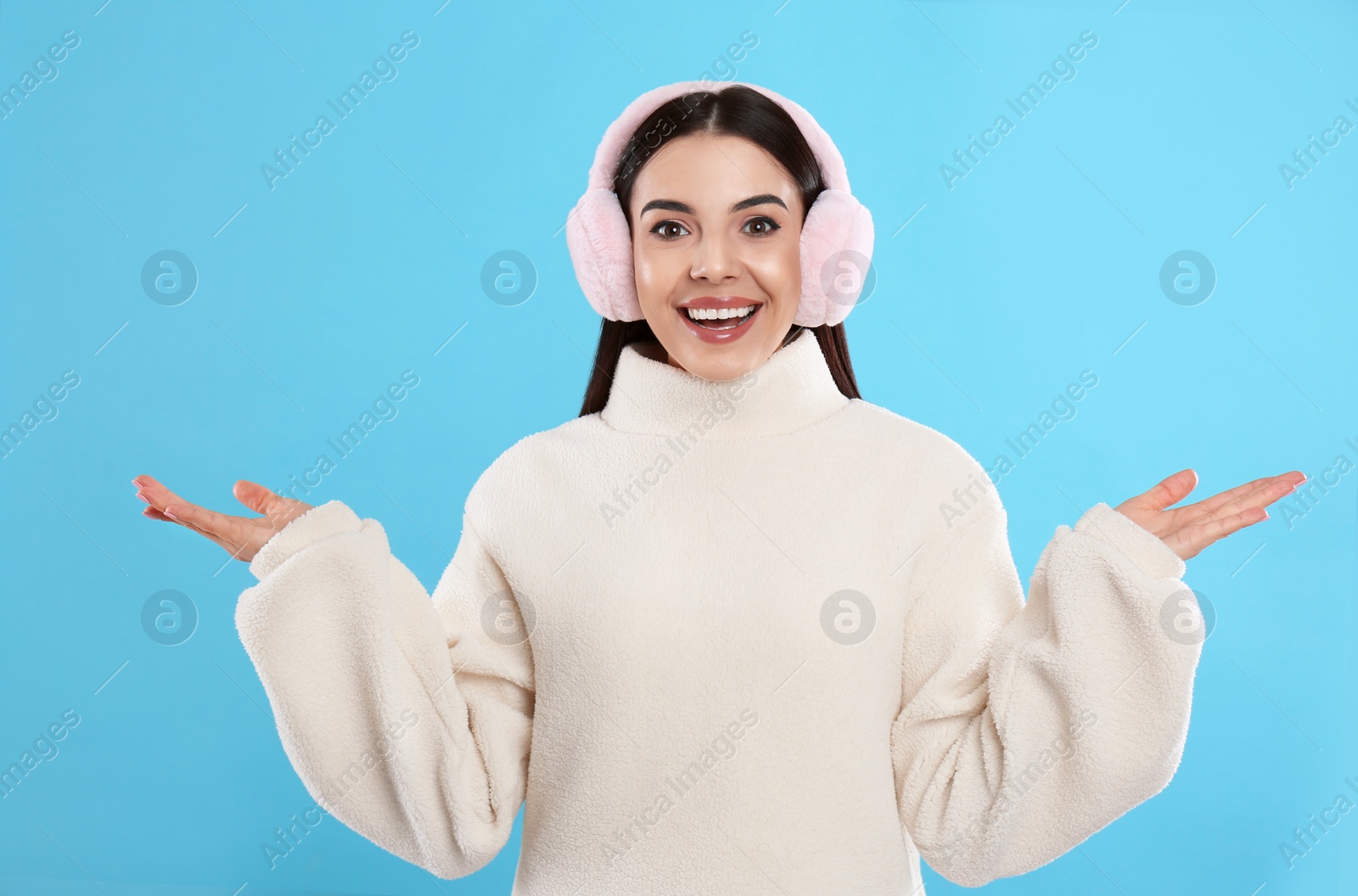 Beautiful young woman wearing earmuffs on light blue background Photo of Beautiful young woman wearing earmuffs on light blue background