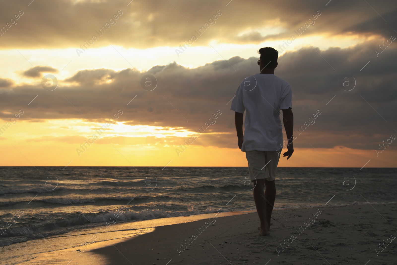 Man walking on sandy beach during sunset, back view Photo of Man walking on sandy beach during sunset, back view