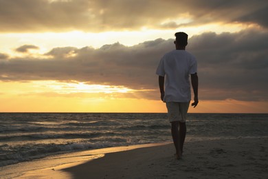 Man walking on sandy beach during sunset, back view Photo of Man walking on sandy beach during sunset, back view