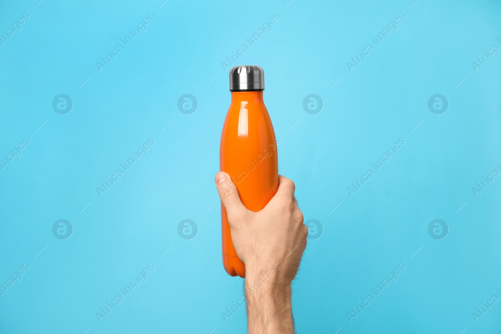Man holding orange thermos bottle on light blue background, closeup Photo of Man holding orange thermos bottle on light blue background, closeup