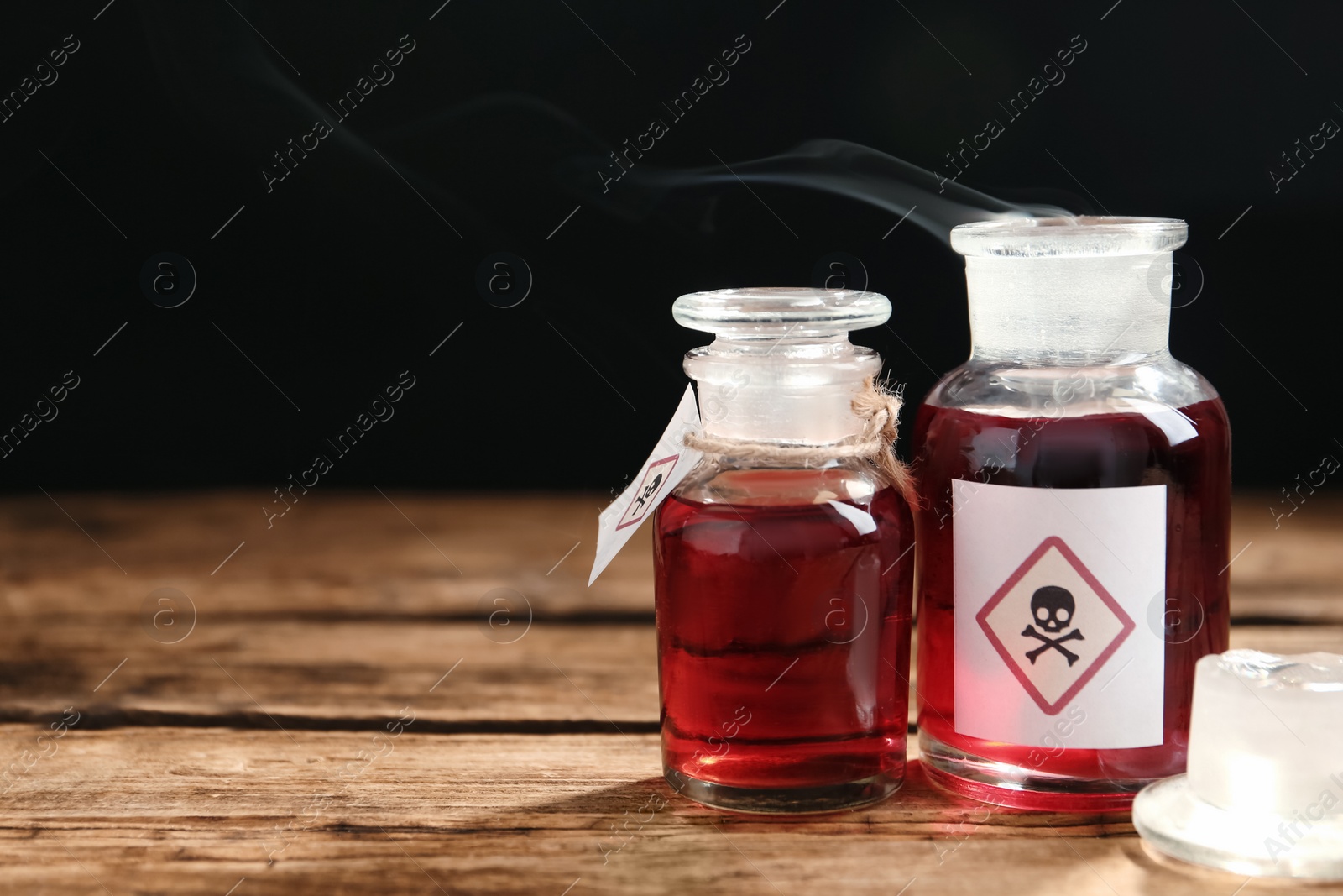 Photo of Glass bottles of poison with warning signs on wooden table. Space for text