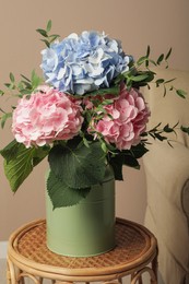 Beautiful hortensia flowers in can on wicker stand indoors Photo of Beautiful hortensia flowers in can on wicker stand indoors