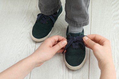 Mother helping son to tie shoe laces at home, closeup Photo of Mother helping son to tie shoe laces at home, closeup