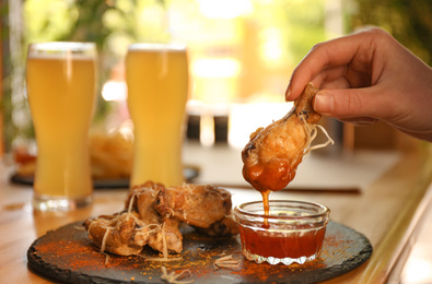 Woman dipping tasty BBQ wing into sauce at table, closeup Photo of Woman dipping tasty BBQ wing into sauce at table, closeup