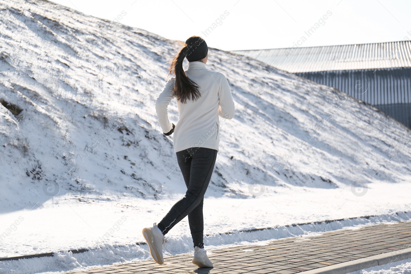 Woman running past snowy hill in winter, back view. Outdoors sports exercises Photo of Woman running past snowy hill in winter, back view. Outdoors sports exercises
