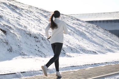 Woman running past snowy hill in winter, back view. Outdoors sports exercises Photo of Woman running past snowy hill in winter, back view. Outdoors sports exercises