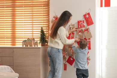 Mother and son taking gift from Advent calendar at home, back view. Christmas tradition Photo of Mother and son taking gift from Advent calendar at home, back view. Christmas tradition