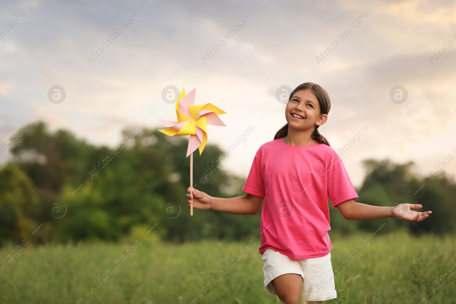 Cute little girl with pinwheel in field, space for text. Child spending time in nature Photo of Cute little girl with pinwheel in field, space for text. Child spending time in nature