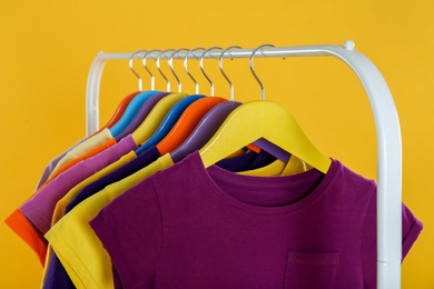 Rack with stylish children clothes on yellow background, closeup Photo of Rack with stylish children clothes on yellow background, closeup