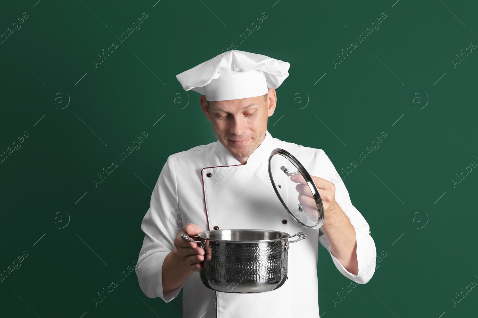 Happy male chef with cooking pot on dark green background Photo of Happy male chef with cooking pot on dark green background
