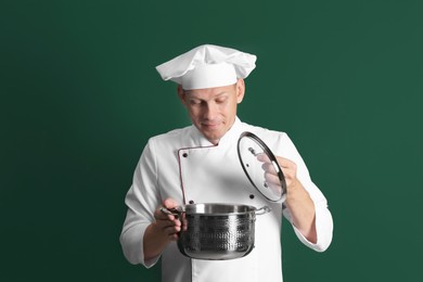 Happy male chef with cooking pot on dark green background Photo of Happy male chef with cooking pot on dark green background