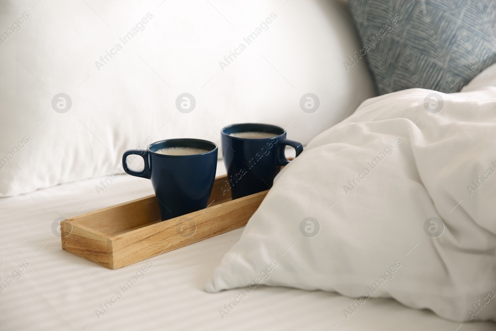 Wooden tray with cups of coffee near soft blanket on bed Photo of Wooden tray with cups of coffee near soft blanket on bed