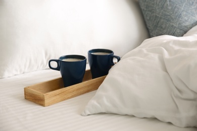 Wooden tray with cups of coffee near soft blanket on bed Photo of Wooden tray with cups of coffee near soft blanket on bed