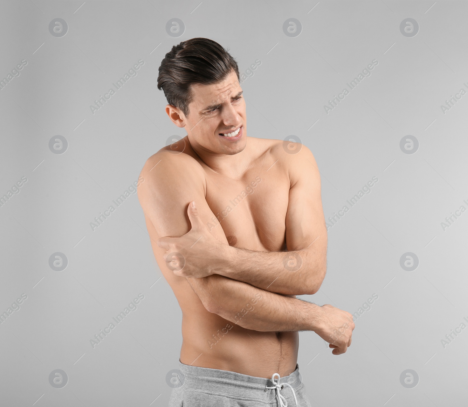 Young man suffering from pain in arm on grey background Photo of Young man suffering from pain in arm on grey background