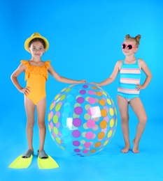 Cute little children in beachwear with inflatable ball on light blue background Photo of Cute little children in beachwear with inflatable ball on light blue background