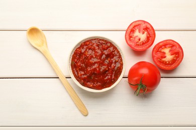 Delicious adjika sauce in bowl with spoon and tomatoes on white wooden table, flat lay Photo of Delicious adjika sauce in bowl with spoon and tomatoes on white wooden table, flat lay