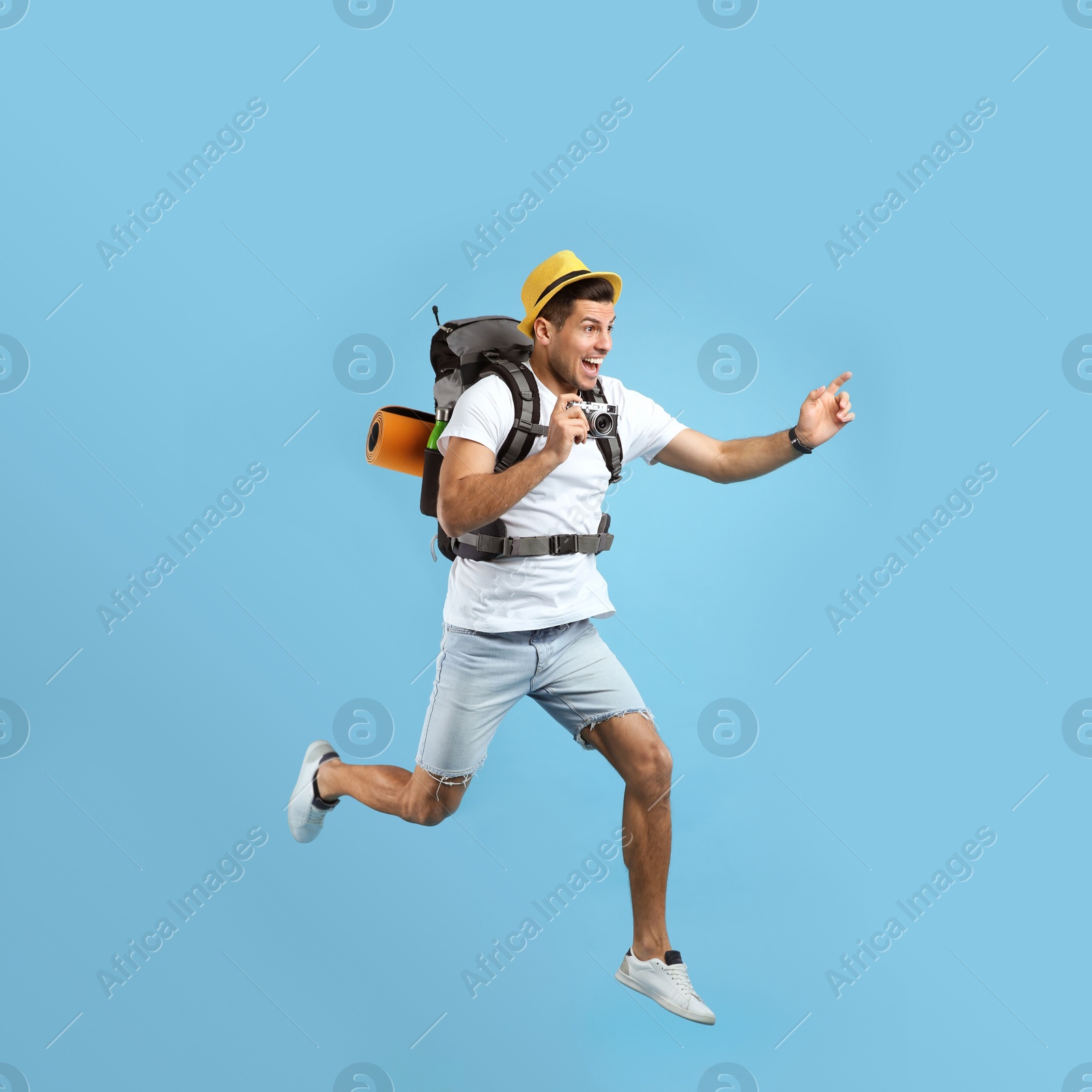 Emotional male tourist with travel backpack and camera jumping on turquoise background Photo of Emotional male tourist with travel backpack and camera jumping on turquoise background