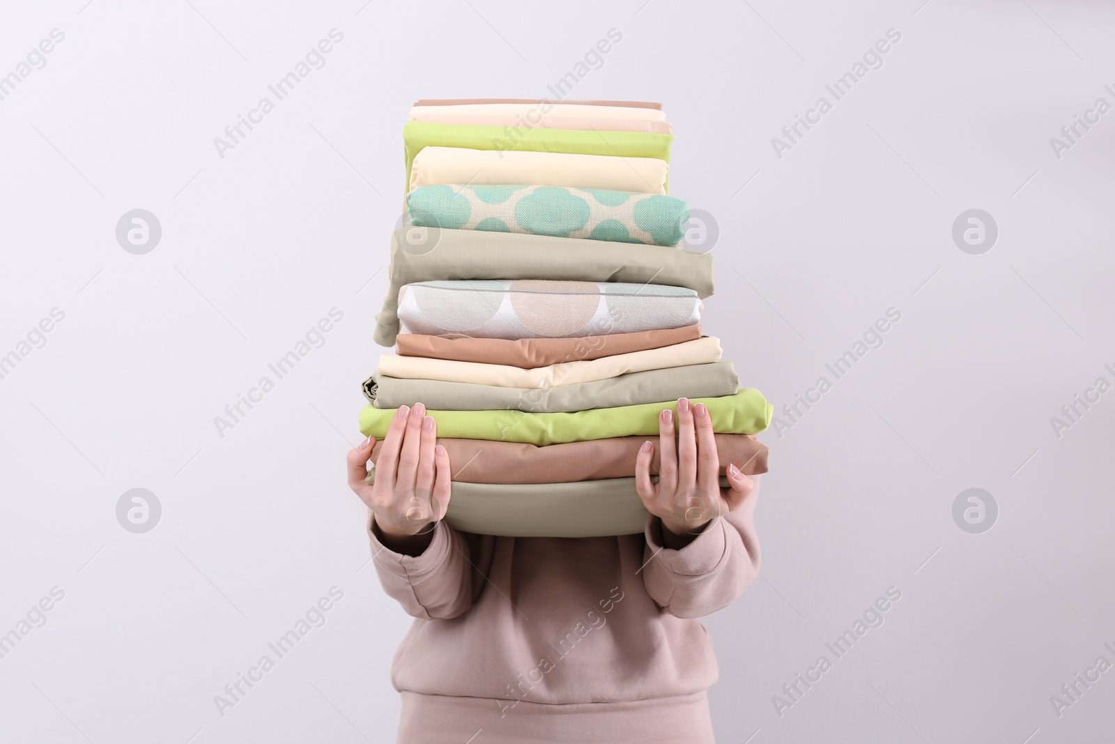Woman holding stack of clean bed linens on light background Photo of Woman holding stack of clean bed linens on light background