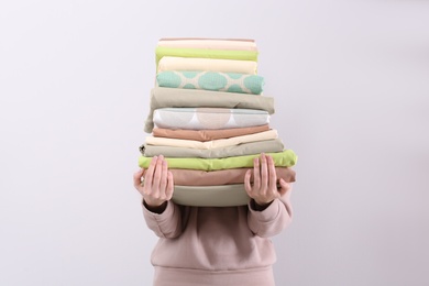 Woman holding stack of clean bed linens on light background Photo of Woman holding stack of clean bed linens on light background