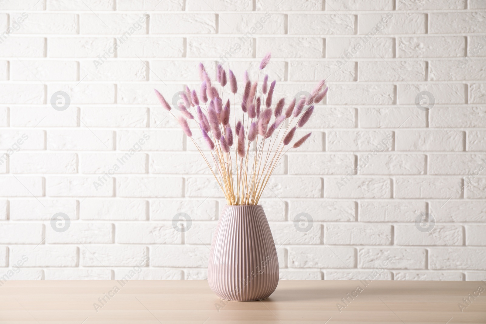 Dried flowers in vase on table against white brick wall Photo of Dried flowers in vase on table against white brick wall