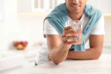 Man holding glass of pure water at table in kitchen, closeup Photo of Man holding glass of pure water at table in kitchen, closeup