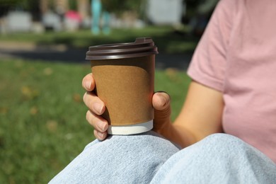 Woman holding takeaway cardboard coffee cup with plastic lid in park, closeup Photo of Woman holding takeaway cardboard coffee cup with plastic lid in park, closeup
