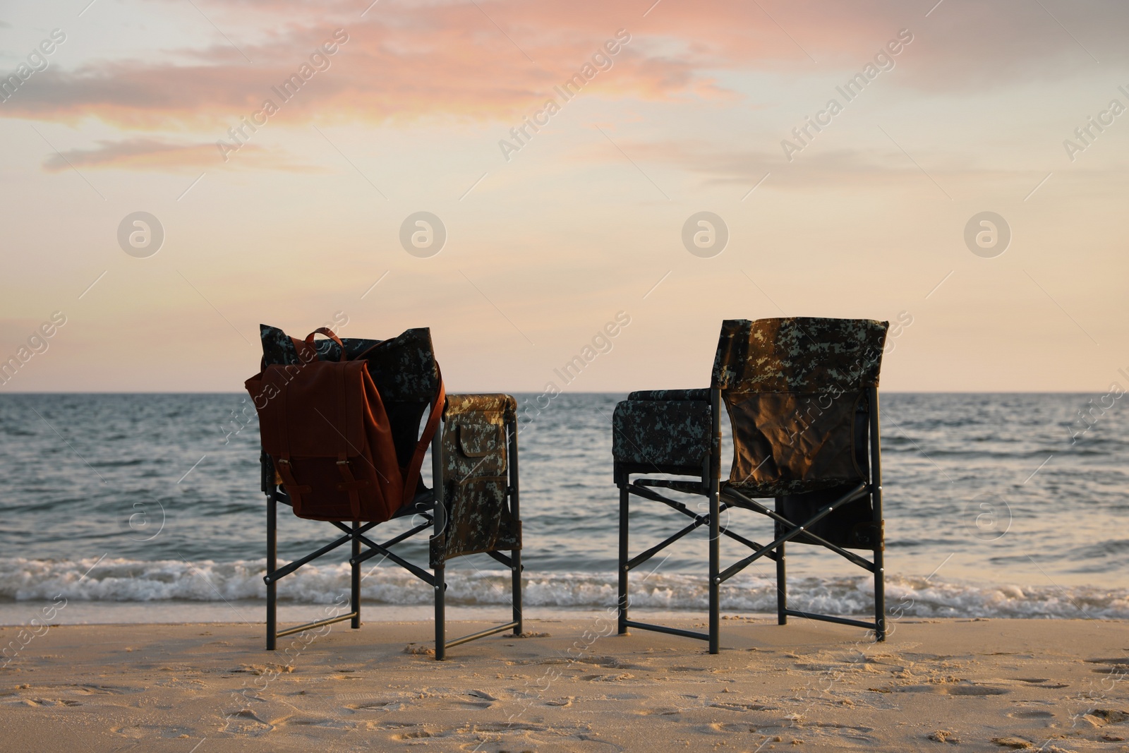 Camping chairs and backpack on sandy beach near sea Photo of Camping chairs and backpack on sandy beach near sea