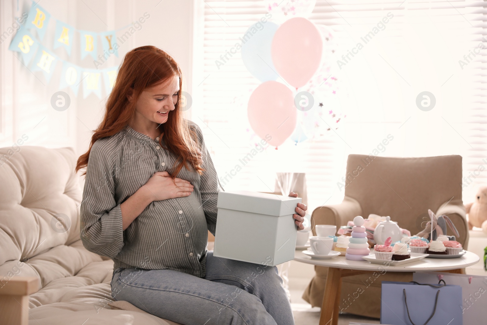 Happy pregnant woman with gift box in room decorated for baby shower party Photo of Happy pregnant woman with gift box in room decorated for baby shower party