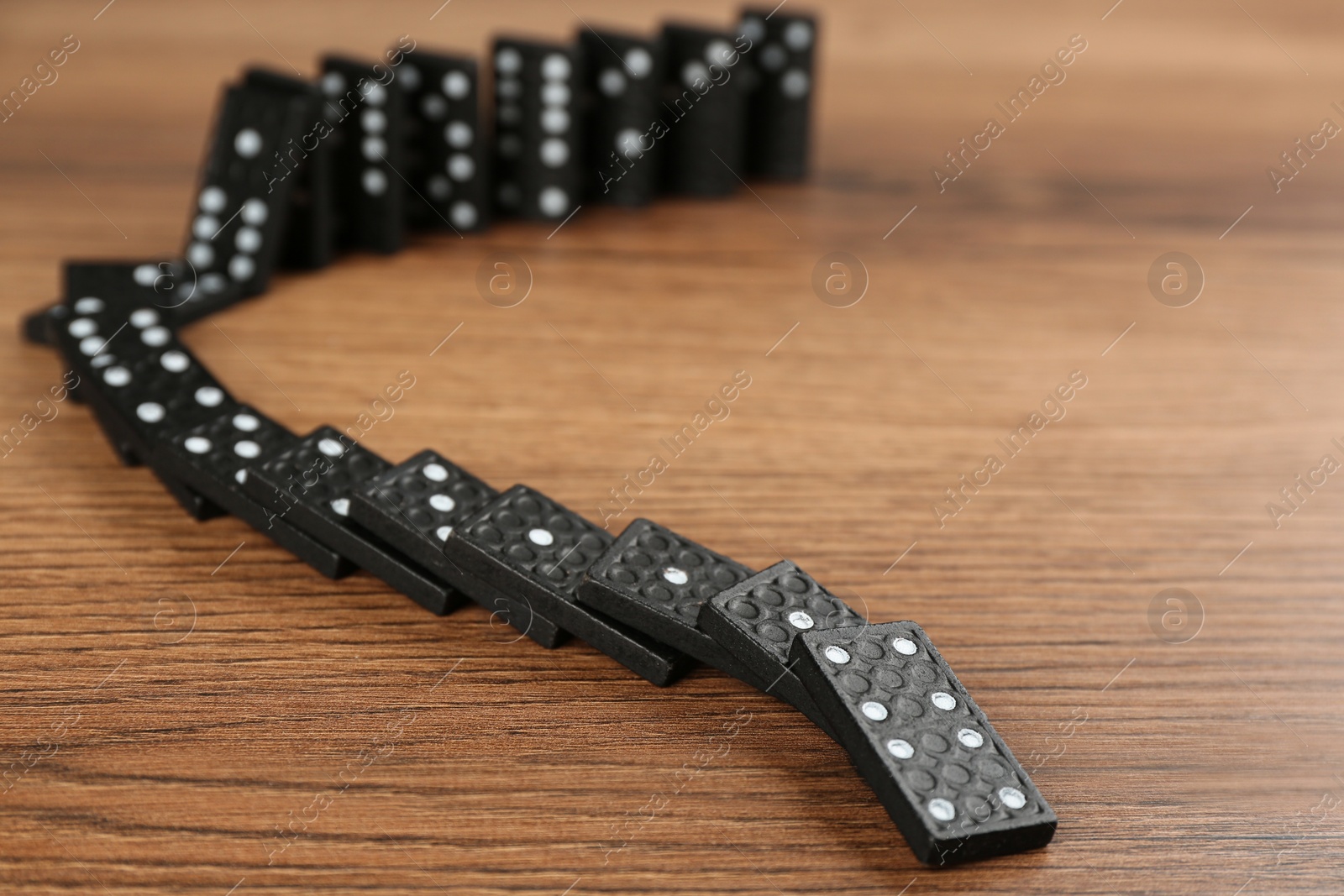 Black domino tiles falling on wooden table Photo of Black domino tiles falling on wooden table